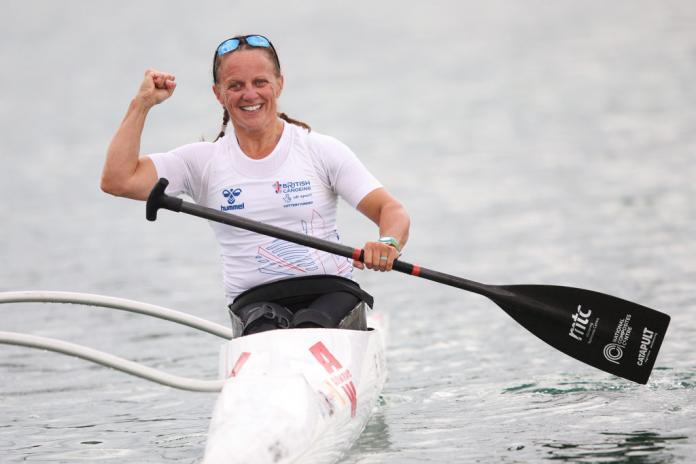 Emma Wiggs, a British Para canoe athlete, pumps her fist after a race. She is holding a paddle with her left hand while sitting in a boat.