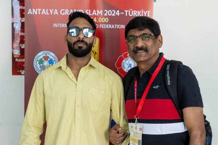 A male Para athlete and his coach stand in front of a banner of the Antalya Grand Slam event in Turkiye