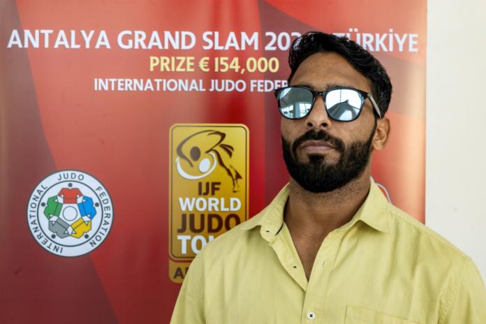 A male Para athlete stands in front of a banner of the Antalya Grand Slam event in Turkiye