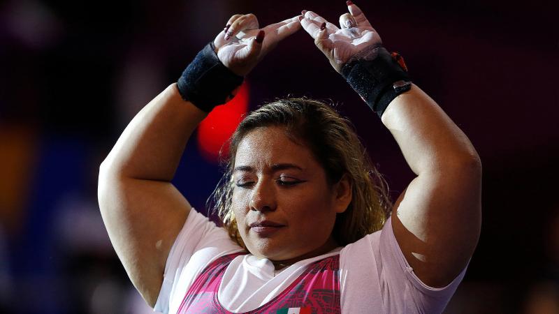 a female powerlifter raises her arms above her head in preparation for her lift