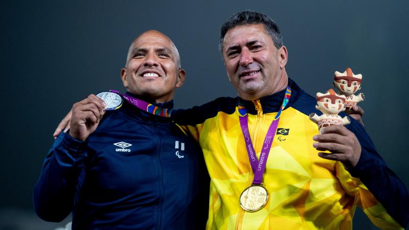 two male Para athletes on the podium with their arms round eachother holding their medals