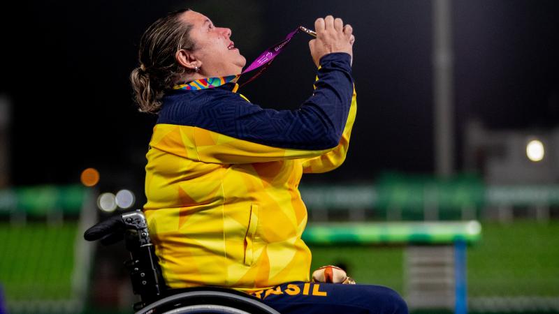a female wheelchair athlete holds up her gold medal to the sky