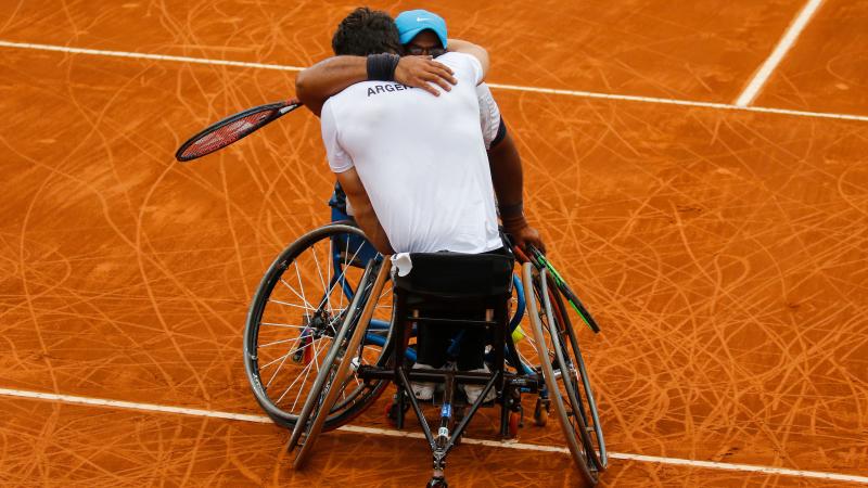 two male wheelchair tennis players hug on the court