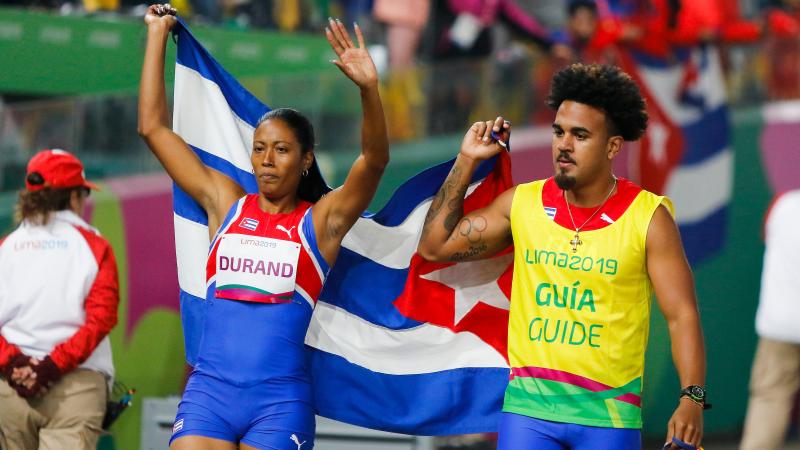 a female vision impaired runner and her male guide hold up the Cuba flag and wave