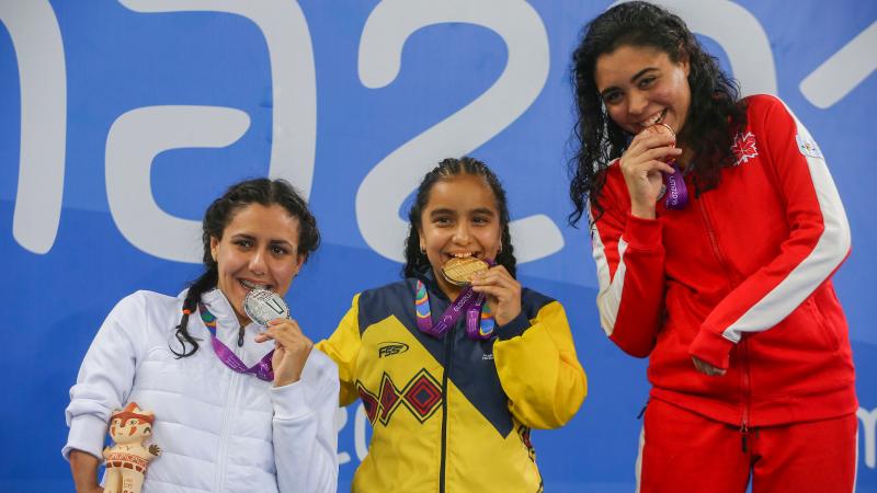 three female Para swimmers on the podium biting their medals