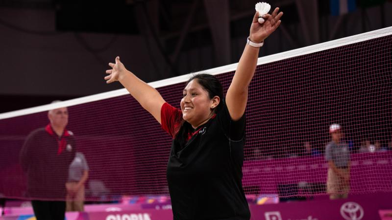 a female wheelchair badminton player throws her arms up in victory