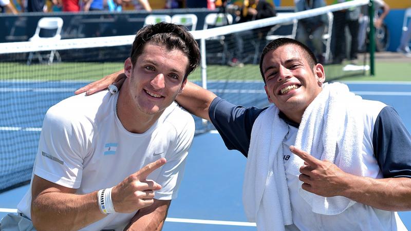 two tennis players smiling to the camera and pointing their index finger making a number 1 sign