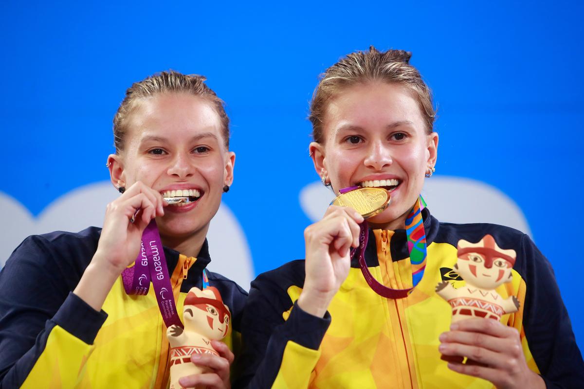 two female Para swimmers on the podium biting their medals