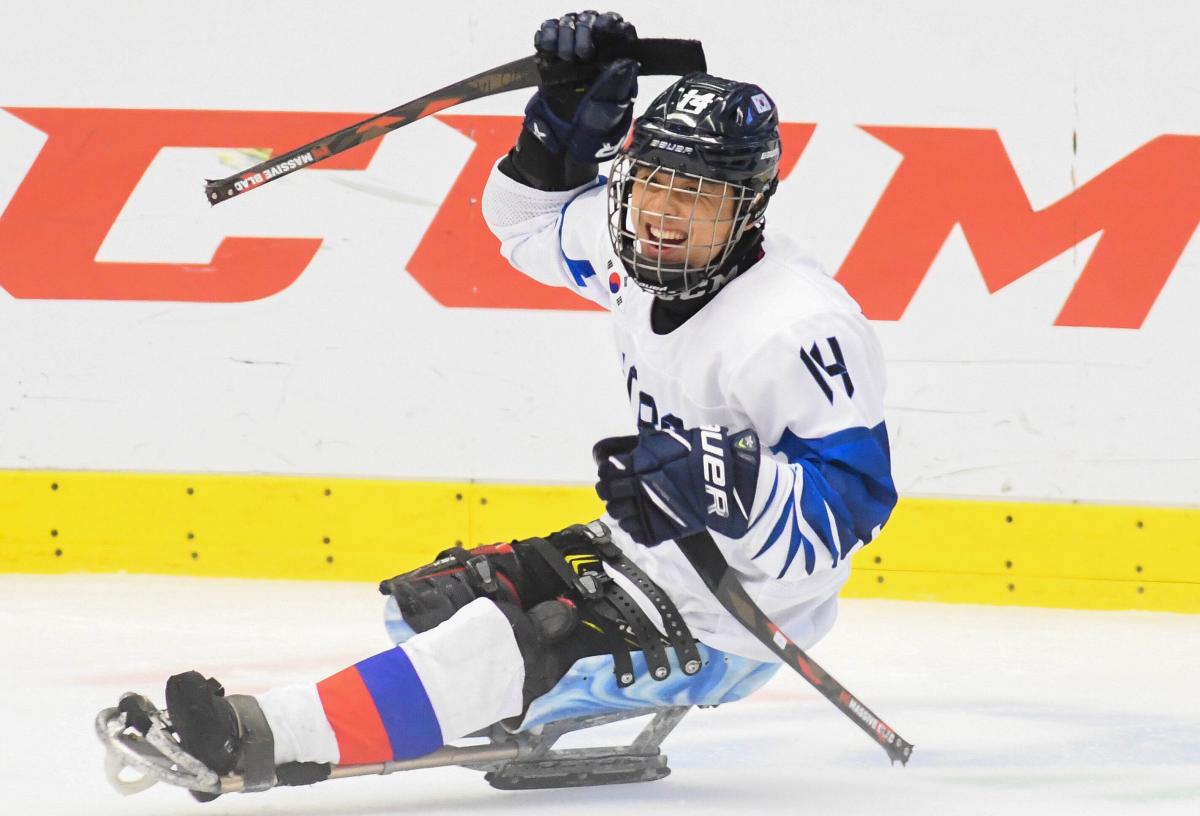 A Para ice hockey player on a sledge celebrates with his right arm raised.