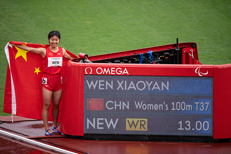 Xiaoyan Wen stands draped in flag of China next to board confirming world record in 100m