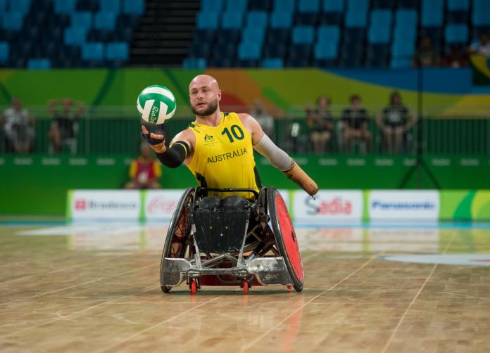 Male wheelchair rugby player tries to grip the ball