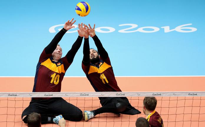 Two male sitting volleyball players try to hit the ball in the air