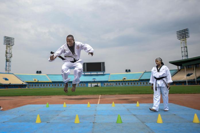 Black male taekwondo athlete jumps over cones as female African coach watches 