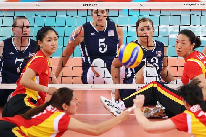 Chinese women sitting volleyball players dive to save the ball as US athletes watch