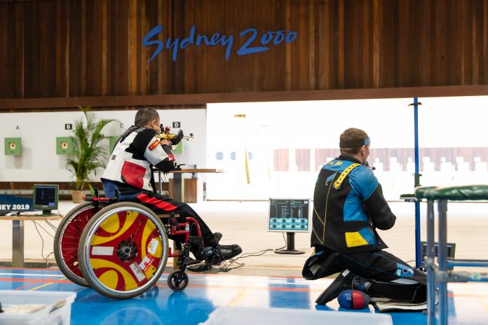 Man kneels to shoot next to another man in a wheelchair in shooting Para sport
