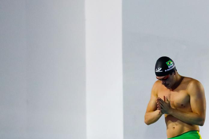 A male swimmer in a Brazilian swim cap puts his hands together, as if in prayer, as he prepares for a race.