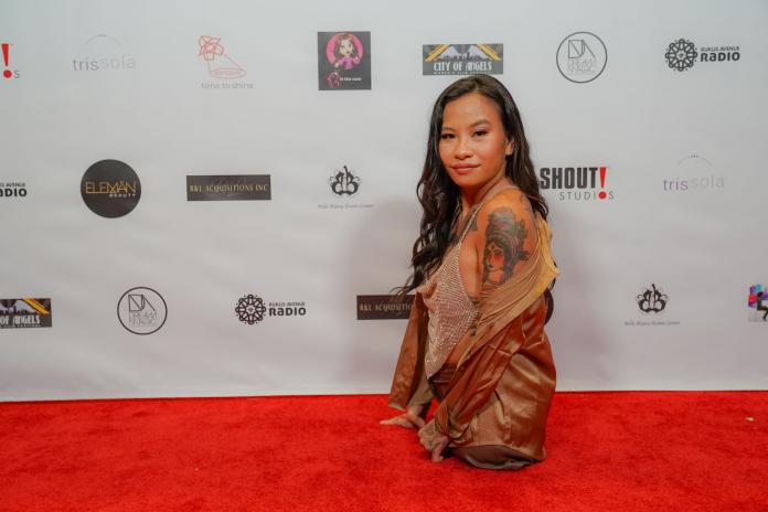 A young female without legs below the hip poses in a glittering dress on the red carpet.