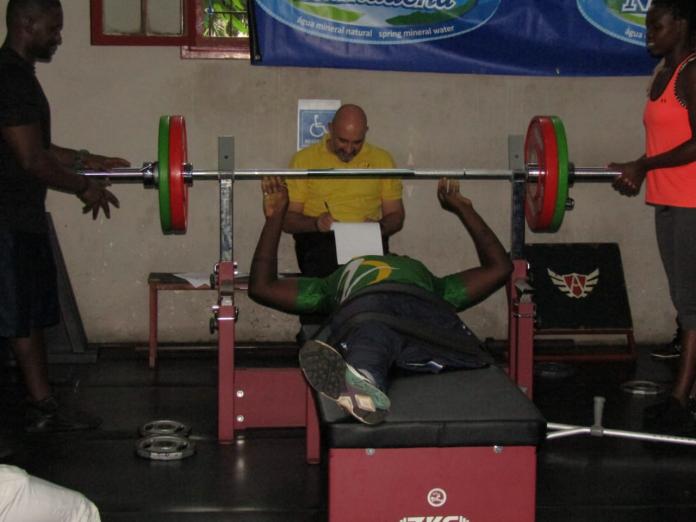 A male Para powerlifter without a left leg above the knee lies on the bench as he prepares to make a lift.