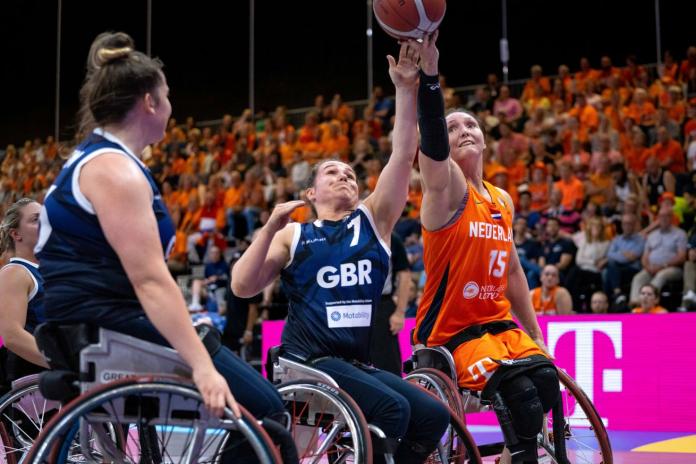 Two wheelchair basketball players reach for a ball during a game