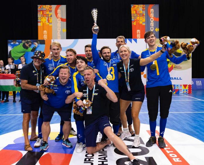 A group of male goalball players celebrate with their trophy and hands in the air 