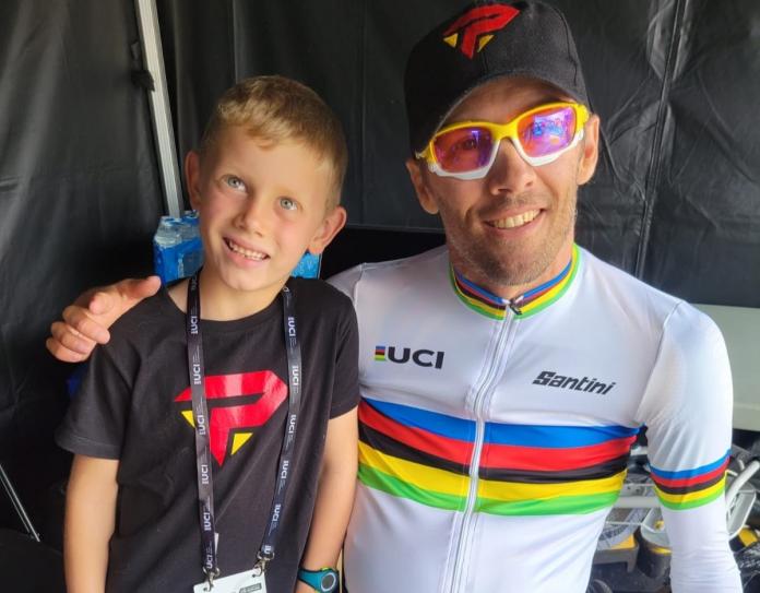 A male athlete wearing the UCI rainbow jersey poses for a photo with his son.
