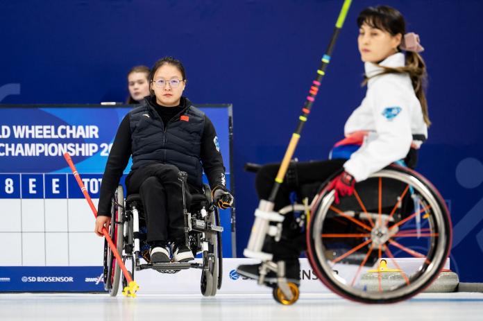 Two female wheelchair curlers in action