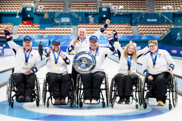 Five wheelchair curlers and a coach pose for a photo