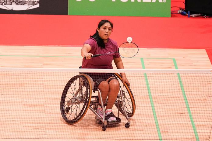 A female Para badminton player, competing in a wheelchair, returns a shuttle during competition.