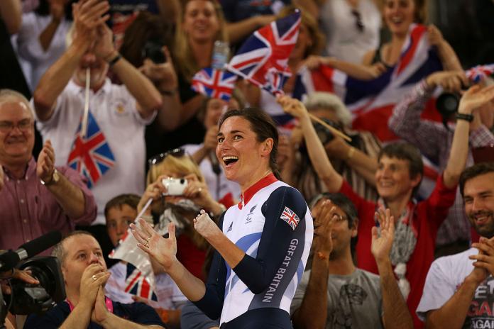 A female Para cyclist celebrates in front of spectators holding the British flag.