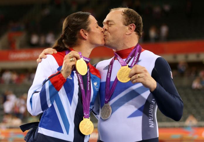A male and female kiss while holding gold medals