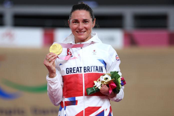 A female Para athlete holds up her gold medal and smiles