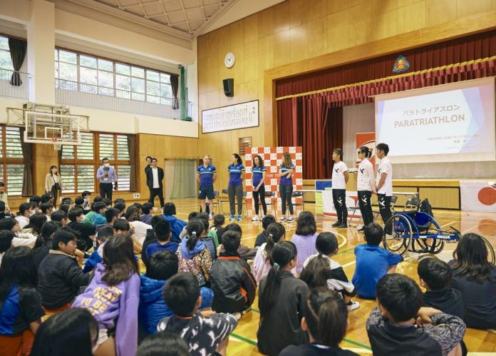 Seven Para triathletes from Ukraine and Japan are giving a presentation about Para triathlon in front of many children.