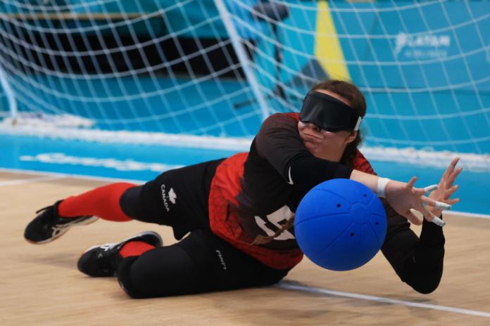 A female goalball player is blocking a blue ball.