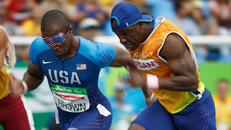 A male blind runner with a USA flag blindfold on sprints alongside his guide