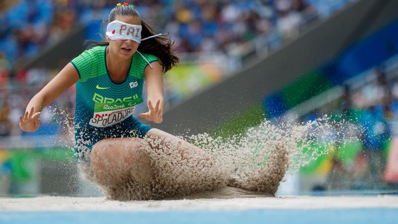 a female long jumper wearing a blindfold jumps into sand