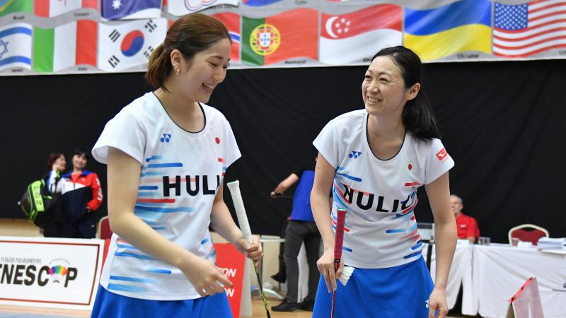 two female standing Para badminton players laughing together on court