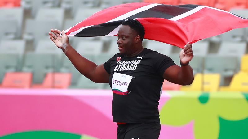 a male Para athlete holding up the Trinidad and Tobago flag