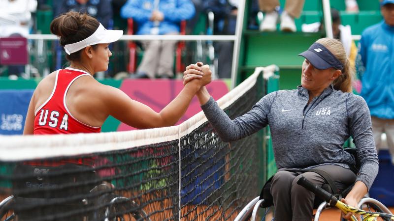 two female wheelchair tennis players high five over the net