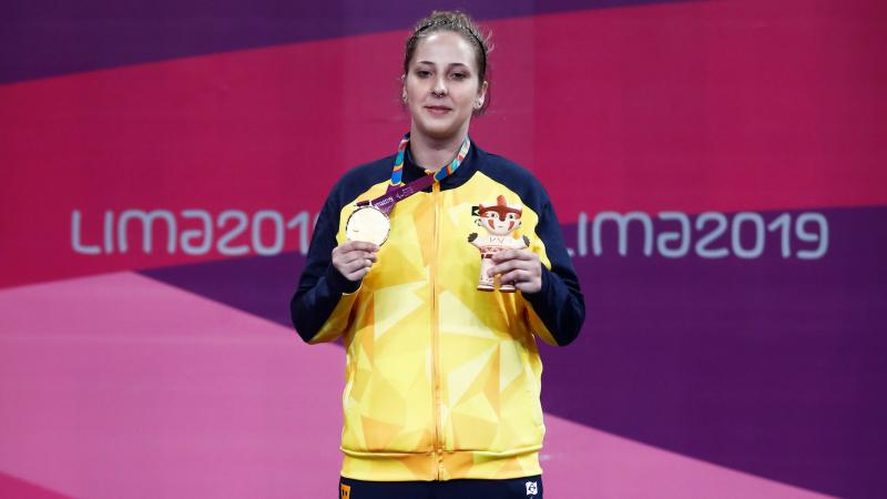 a female Para judoka stands on the podium holding her gold medal