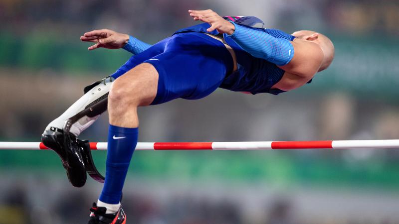 a male Para athlete with a prosthetic leg jumps backwards over a high bar