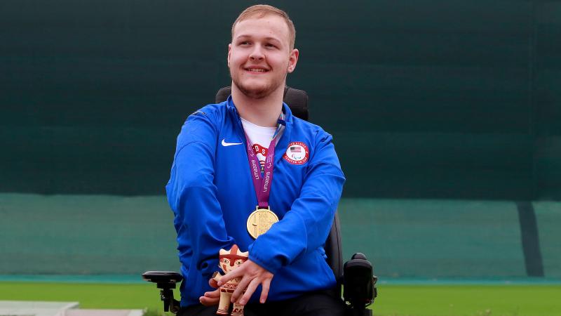a male Para shooter in a wheelchair on the podium with a gold medal