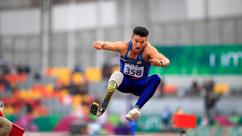 a male Para athlete with a prosthetic leg jumping into a sandpit