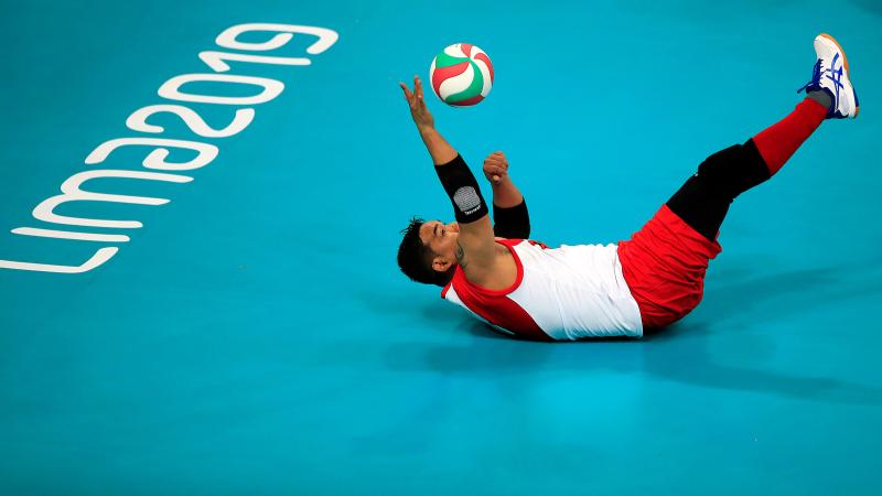 a male sitting volleyball player falls backwards to reach a ball