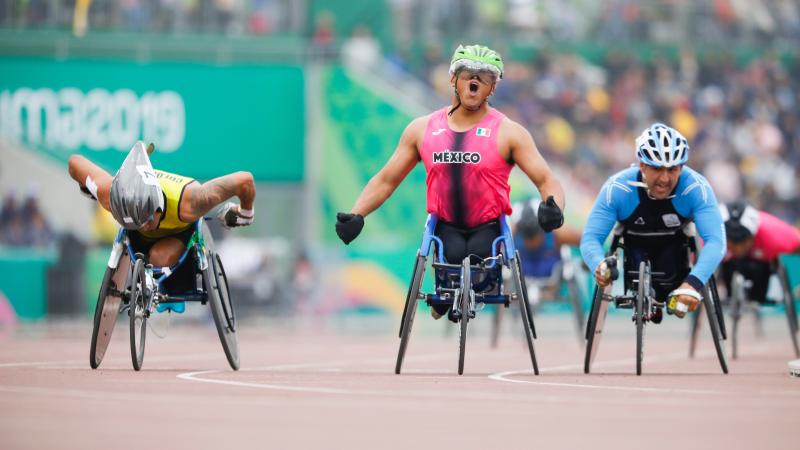 a male wheelchair racer celebrates as he crosses the finish line first