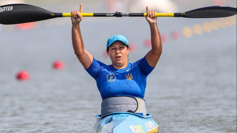 Woman in kayak raises paddle over her head