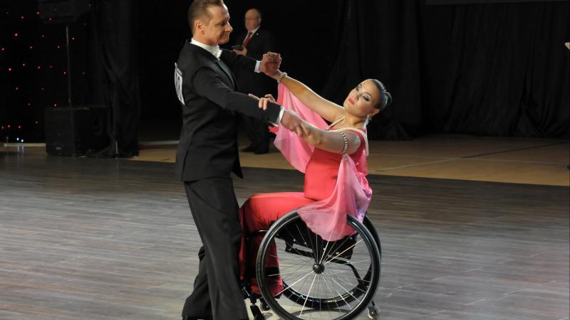 Male standing dancer performs standard dance with female partner in wheelchair