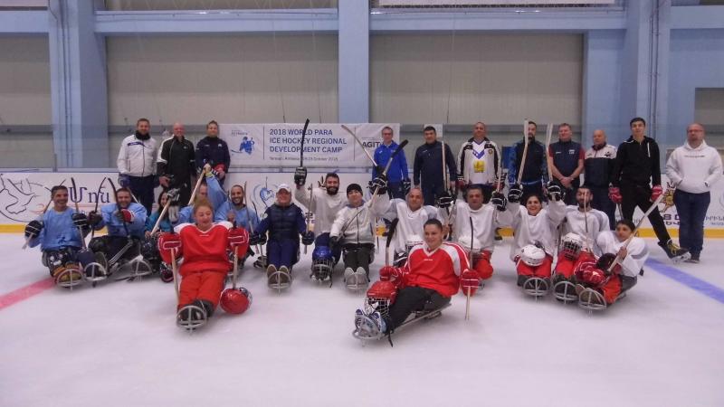 a group of Para ice hockey players sitting on the ice and raising their sticks