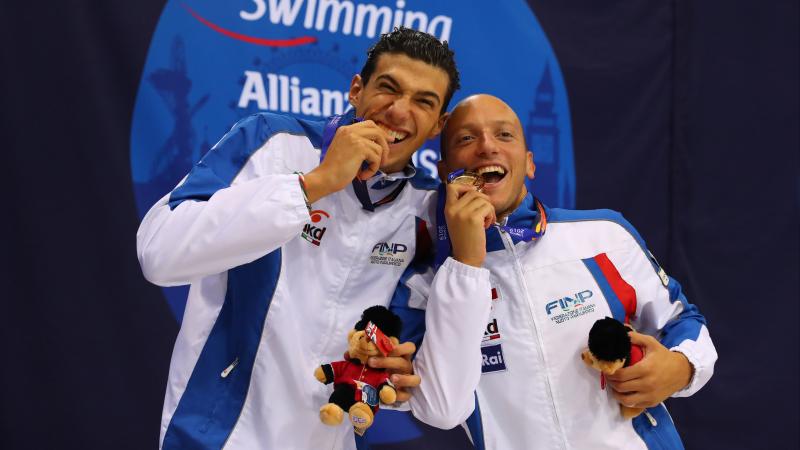 two male Para swimmers biting their medals
