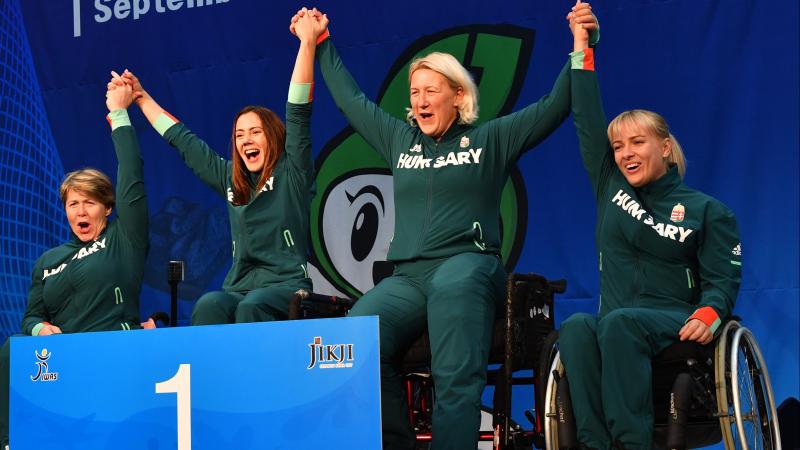 Four Hungarian female wheelchair fencers hold hands on the podium