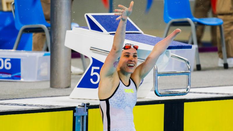 a female Para swimmer raises her arms in celebration in the pool